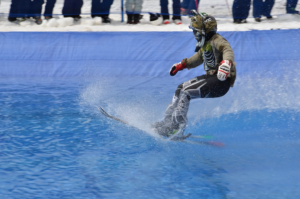 Image of snow skier skimming across a slushy pool of water. 